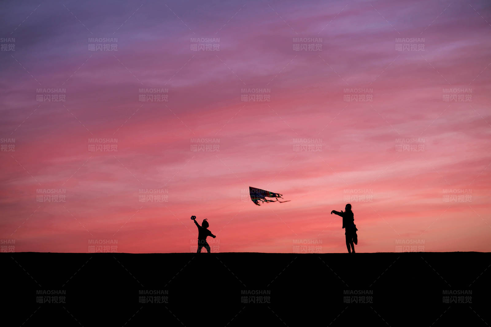 粉色晚霞中放风筝的妈妈和孩子图片