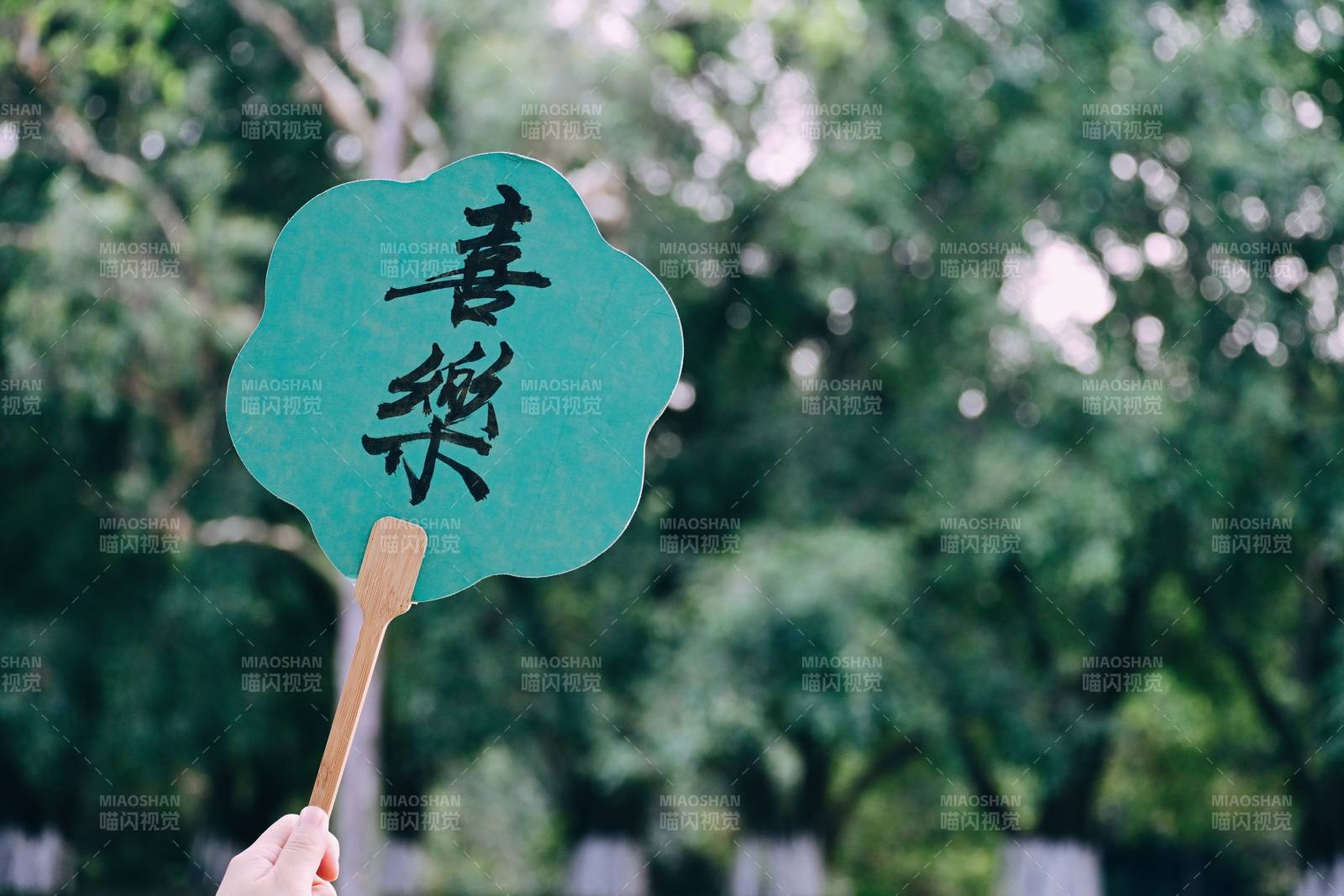 手持绿色扇子在树下图片