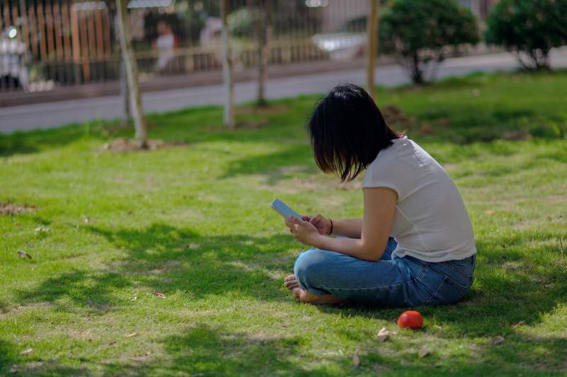 草地上的女孩玩手机图片