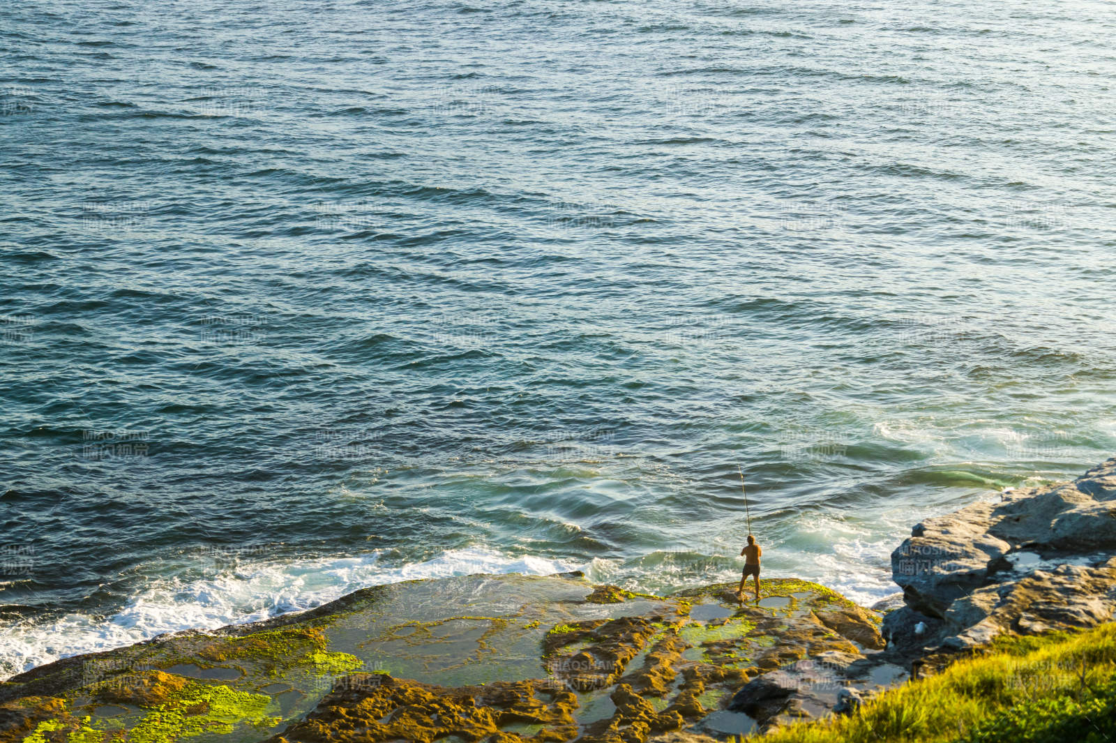 海边岩石上的垂钓者图片