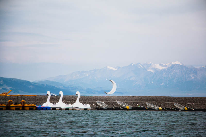 赛里木湖湖畔天鹅船与雪山背景图片