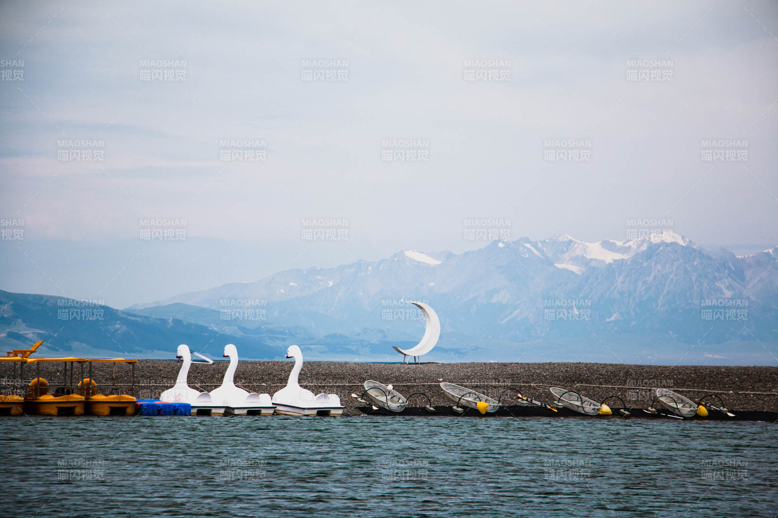 赛里木湖湖畔天鹅船与雪山背景图片