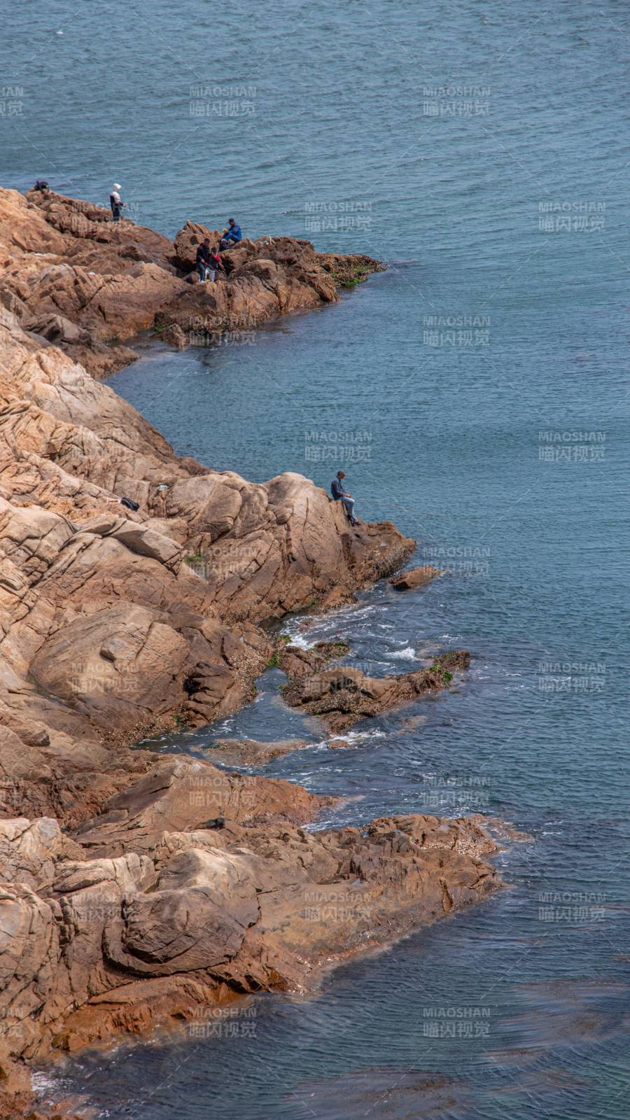 海边岩石上的垂钓者图片
