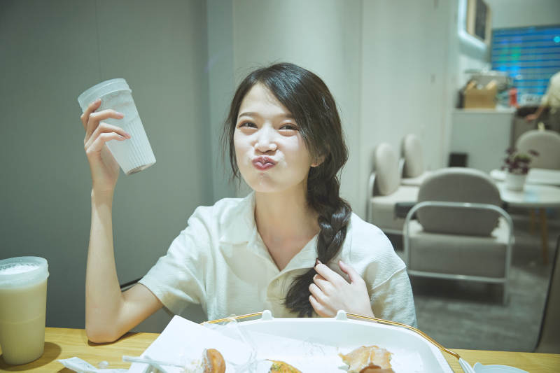 在烘焙店吃面包喝牛奶的可爱亚洲少女图片