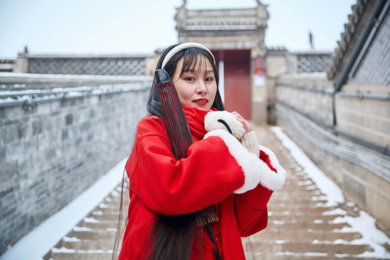 雪后在老城古巷穿着喜庆服饰的亚洲少女图片