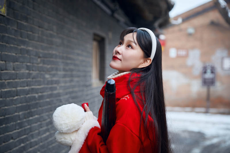 雪后在老城古巷穿着喜庆服饰的亚洲少女图片