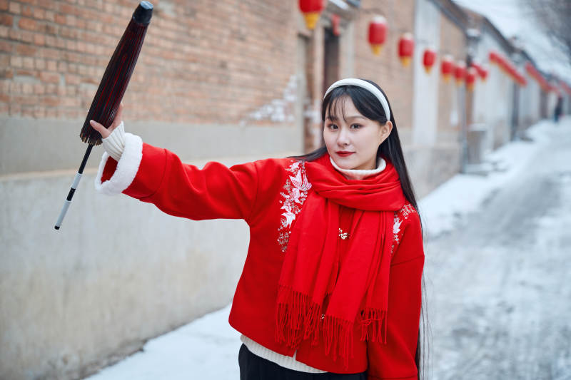 雪后在老城古巷穿着喜庆服饰的亚洲少女图片