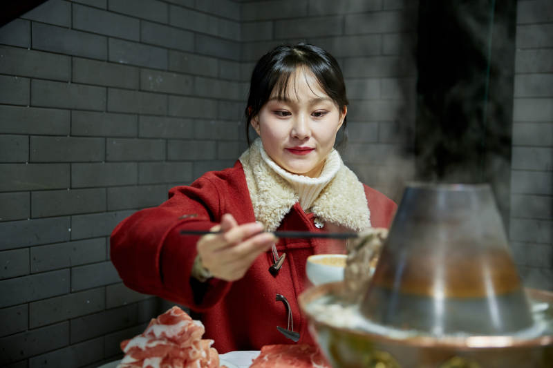 在饭店吃传统铜锅涮肉的亚洲少女图片