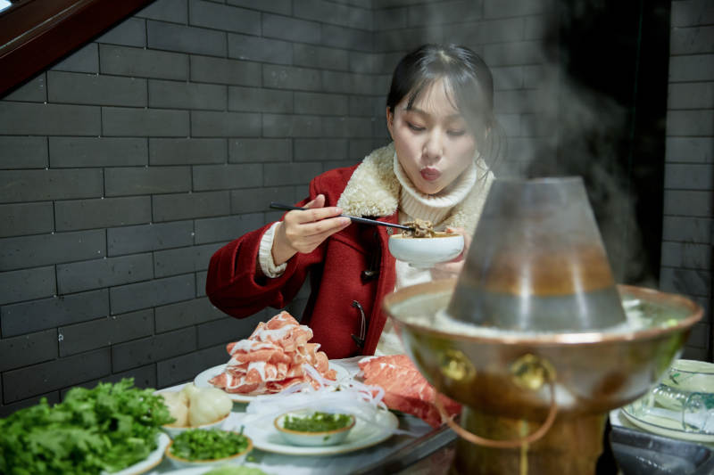 在饭店吃传统铜锅涮肉的亚洲少女图片