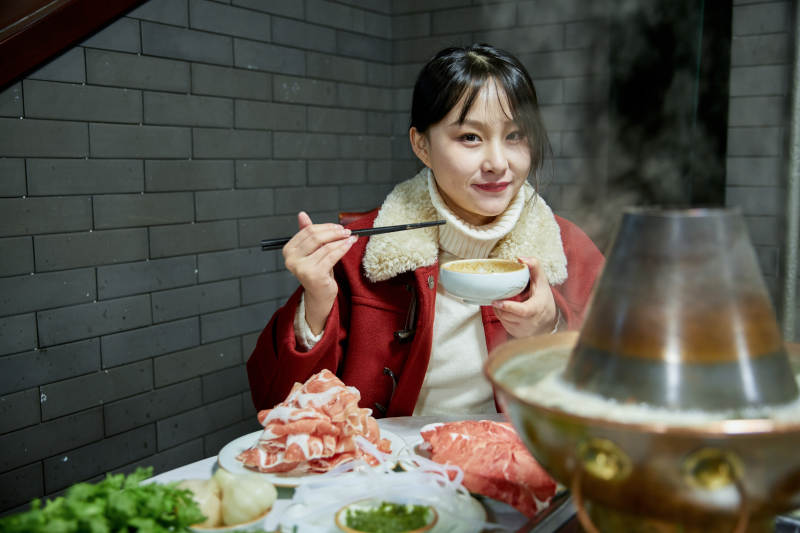 在饭店吃传统铜锅涮肉的亚洲少女图片