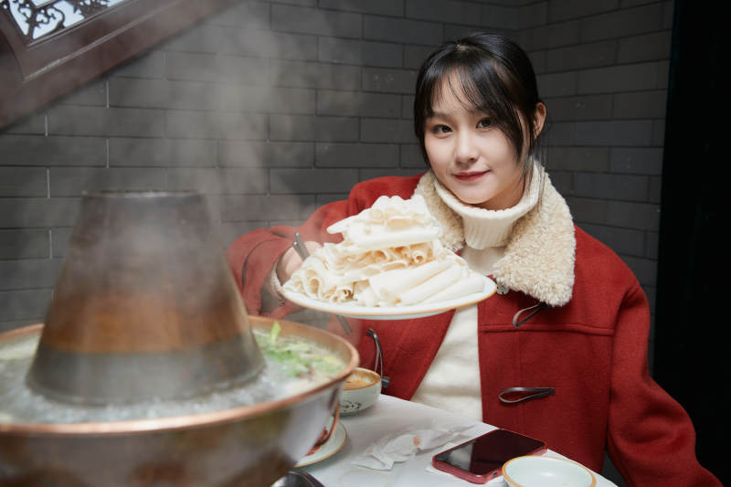 在饭店吃传统铜锅涮肉的亚洲少女图片