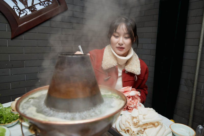 在饭店吃传统铜锅涮肉的亚洲少女图片