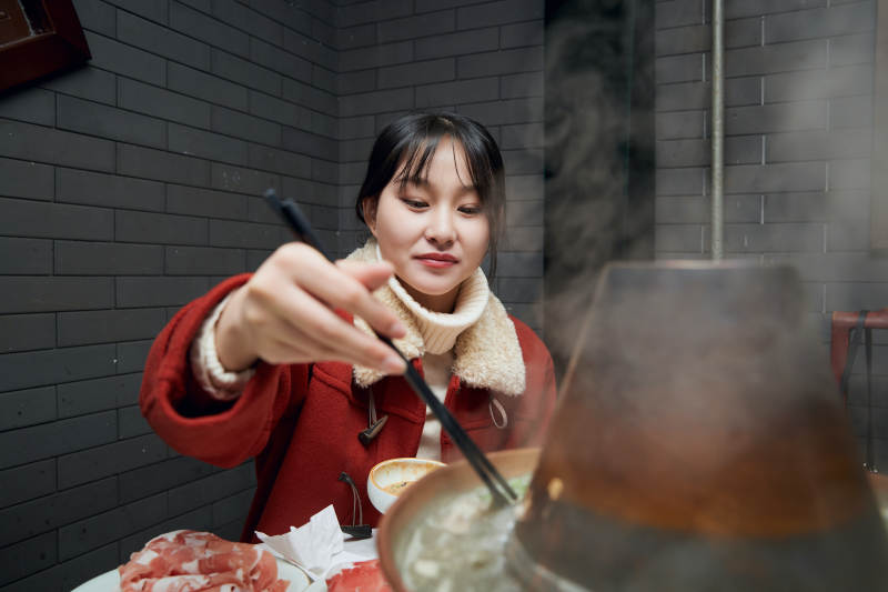 在饭店吃传统铜锅涮肉的亚洲少女图片