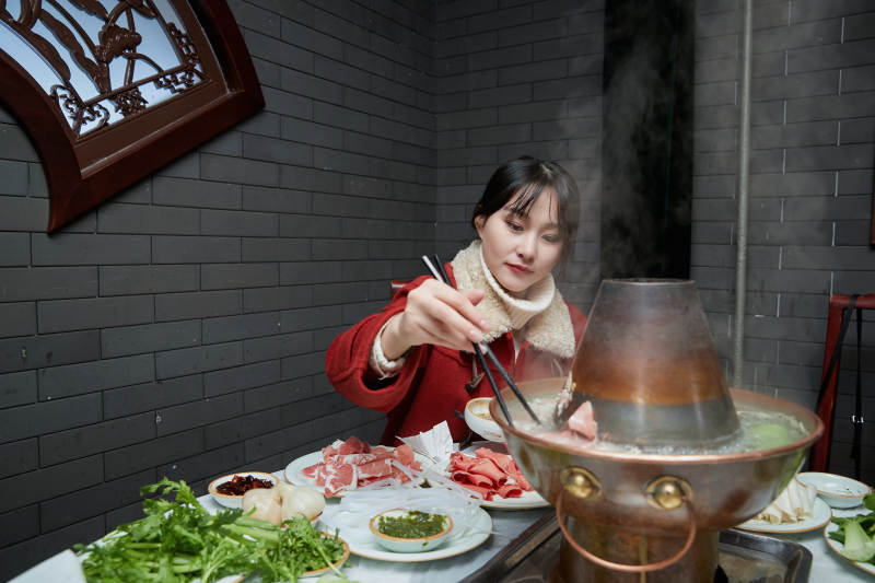 在饭店吃传统铜锅涮肉的亚洲少女图片