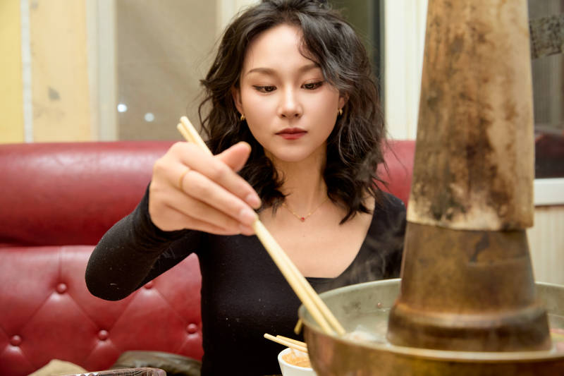 饭店吃传统铜锅涮肉的东方美女图片