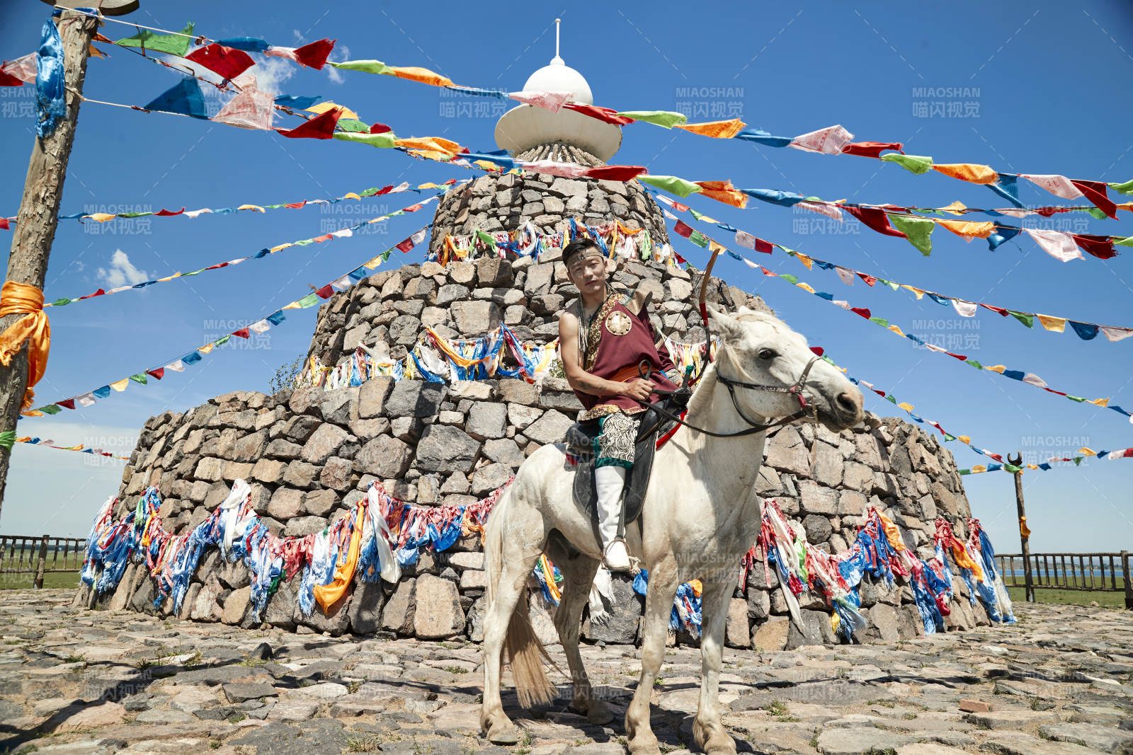 草原敖包前骑马拉弓射箭的蒙古弓箭手图片