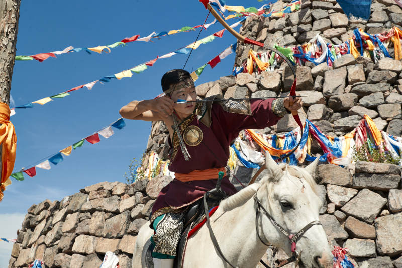 草原敖包前骑马拉弓射箭的蒙古弓箭手图片
