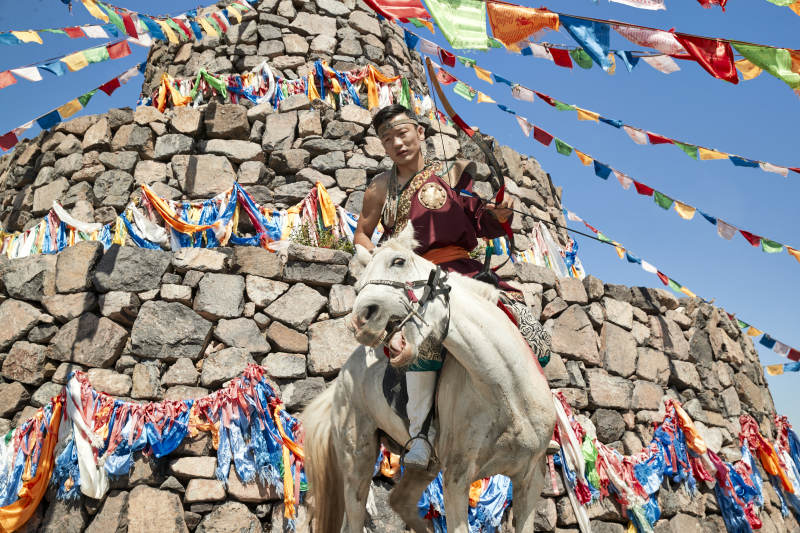 草原敖包前骑马拉弓射箭的蒙古弓箭手图片