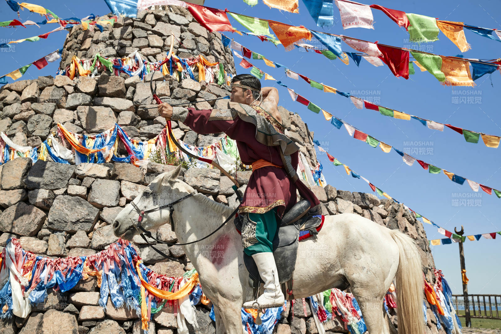 草原敖包前骑马拉弓射箭的蒙古弓箭手图片