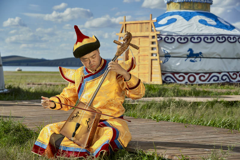 蒙古包前身穿蒙古族服饰拉马头琴的男子图片