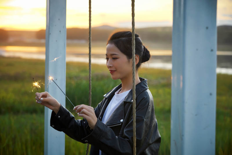 夕阳下湖畔秋千上燃放仙女棒的可爱少女图片