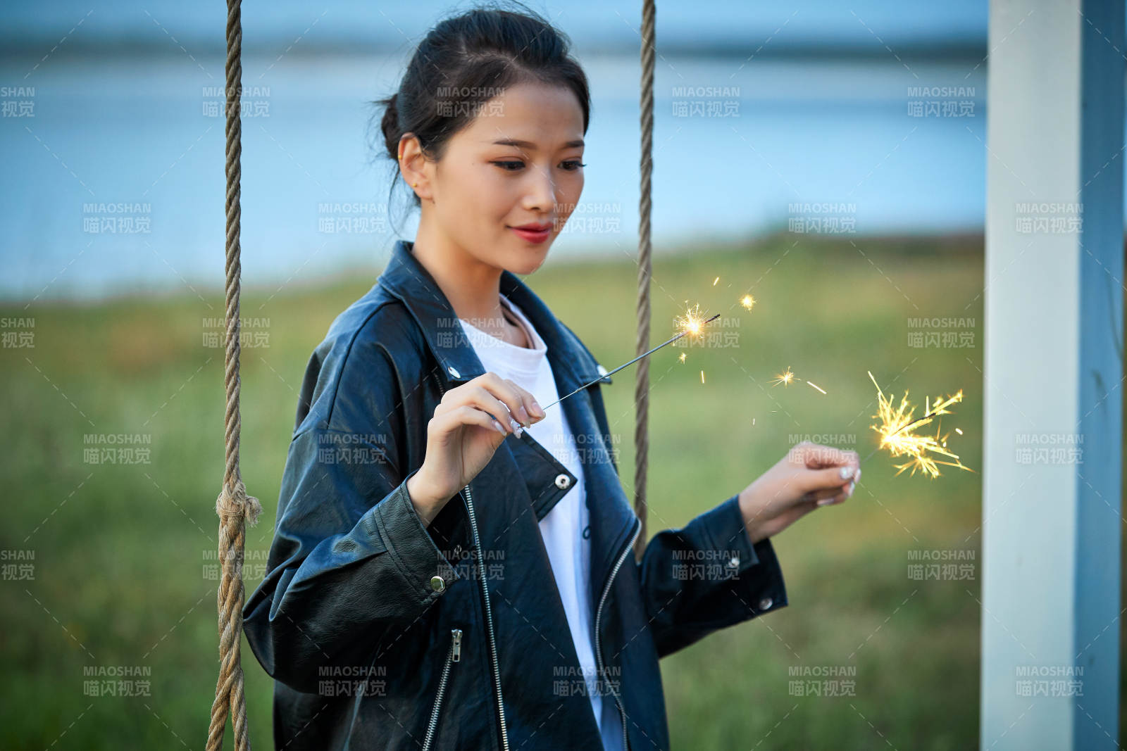 夕阳下湖畔秋千上燃放仙女棒的可爱少女图片