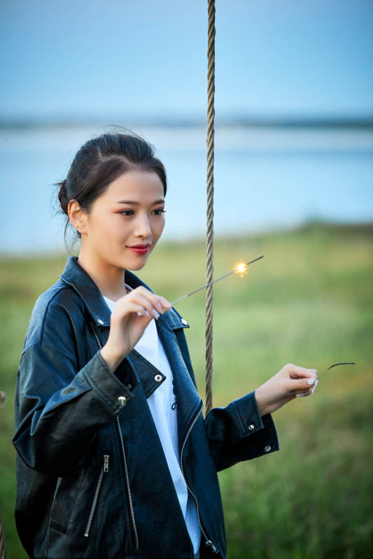 夕阳下湖畔秋千上燃放仙女棒的可爱少女图片