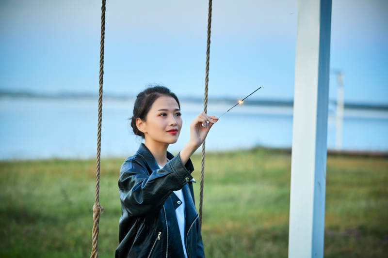 夕阳下湖畔秋千上燃放仙女棒的可爱少女图片