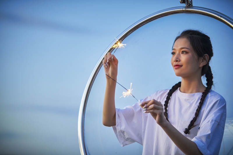 傍晚湖畔透明秋千上燃放仙女棒的可爱少女图片