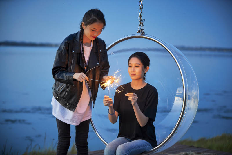 傍晚湖畔透明秋千上燃放仙女棒的可爱少女图片