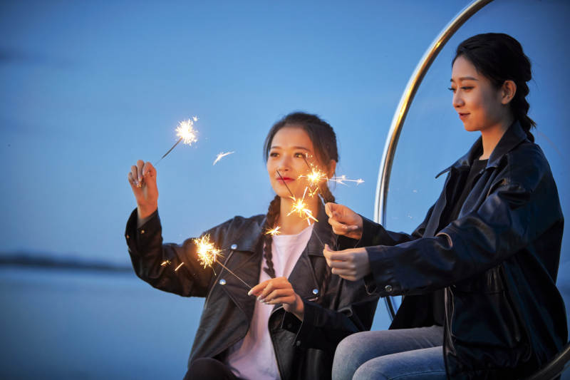 傍晚湖畔透明秋千上燃放仙女棒的可爱少女图片