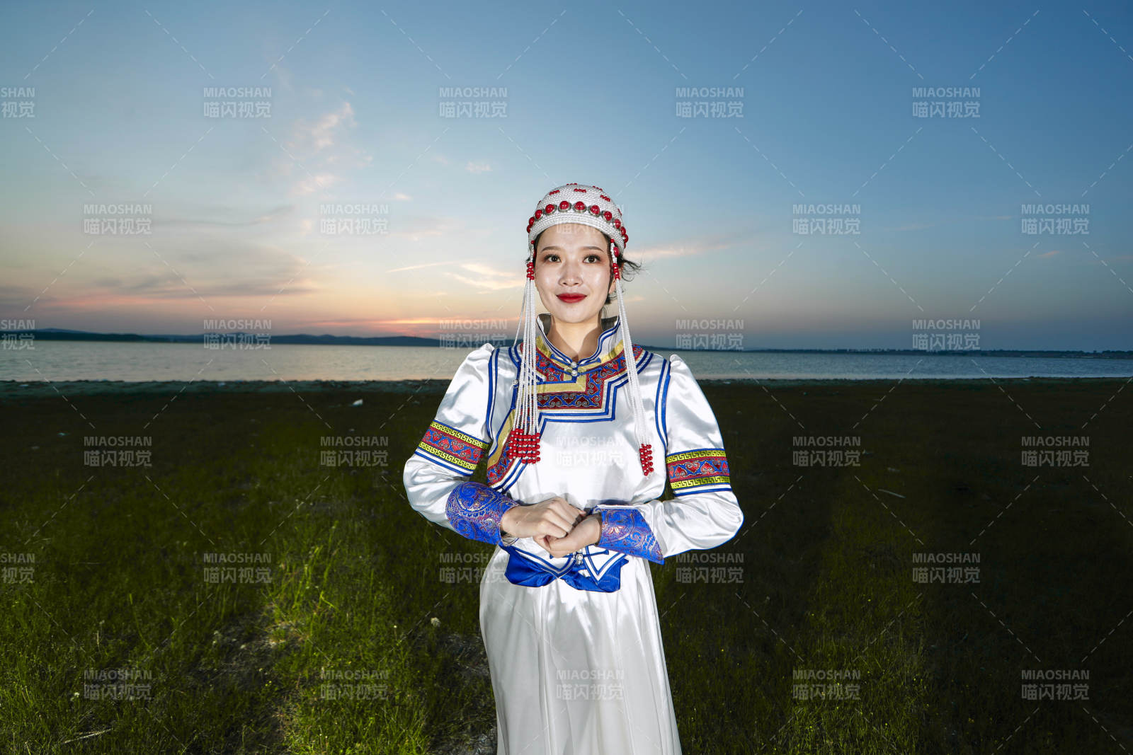 晚霞的草原湖畔穿蒙古族传统服饰的年轻女性图片