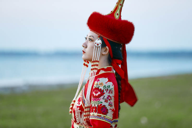晚霞的草原湖畔穿蒙古族传统服饰的年轻女性图片