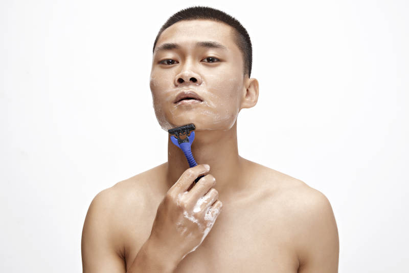 白色背景下手持剃须刀在刮胡子的亚洲男性图片