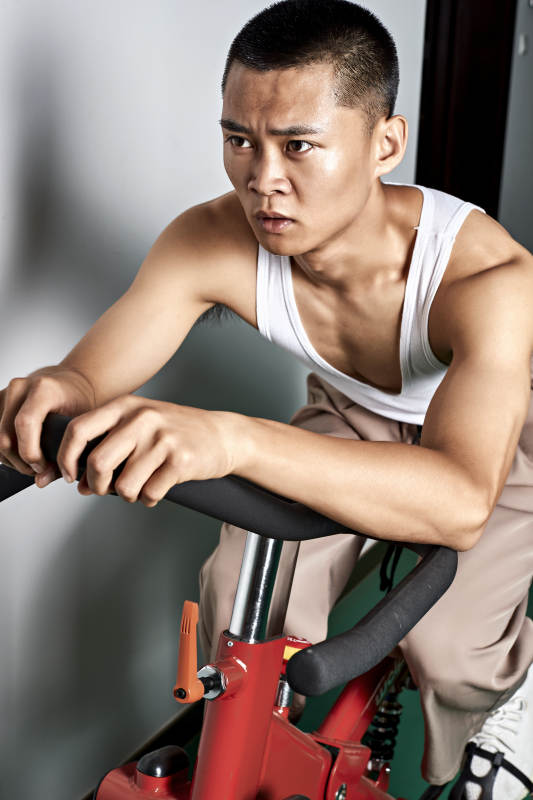 在室内进行动感单车锻炼的亚洲健身男士形象图片