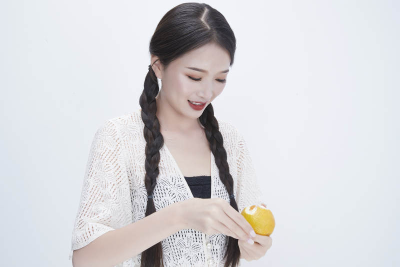 在剥橙子皮的身穿镂空连衣裙的亚洲少女人像图片