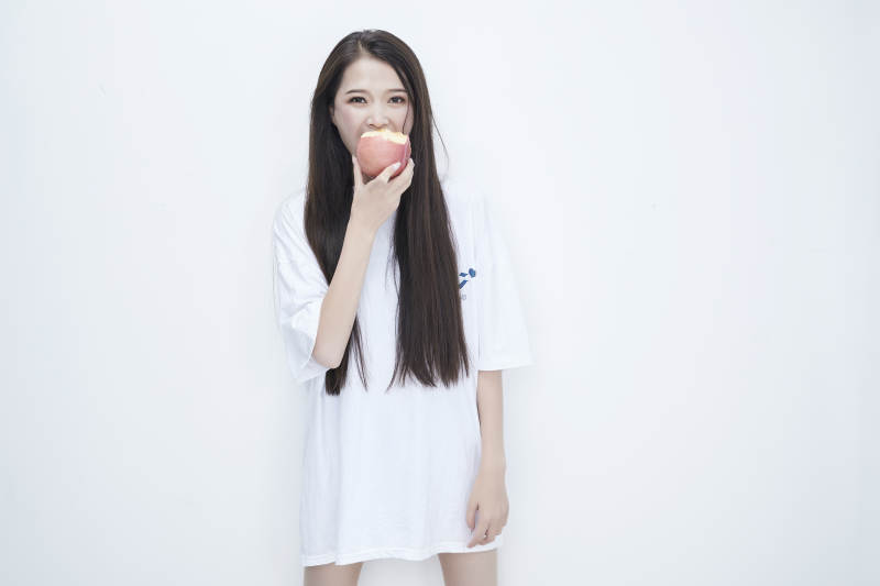 吃苹果的穿白色长T血衫的长发可爱少女人像图片