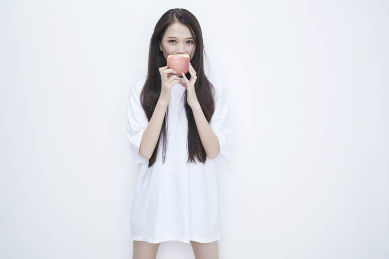吃苹果的穿白色长T血衫的长发可爱少女人像图片