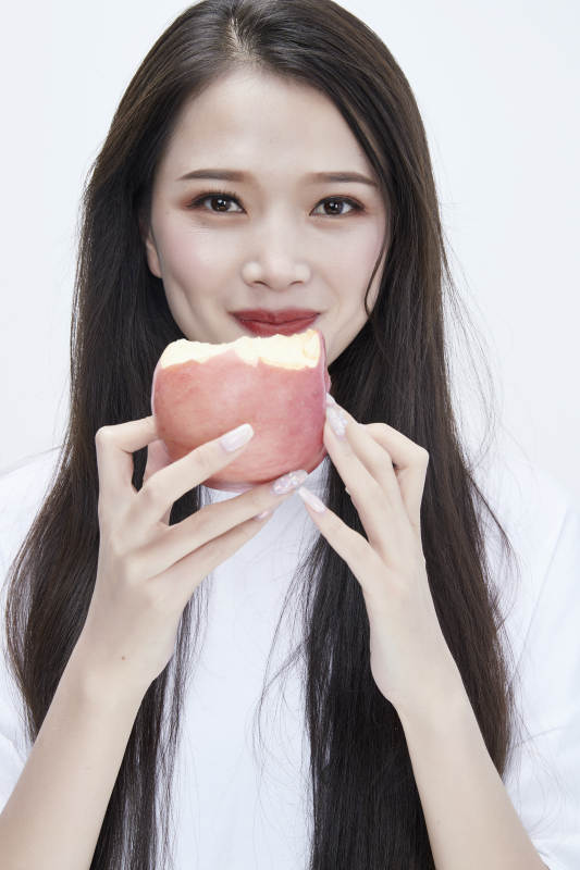 吃苹果的穿白色长T血衫的长发可爱少女人像图片