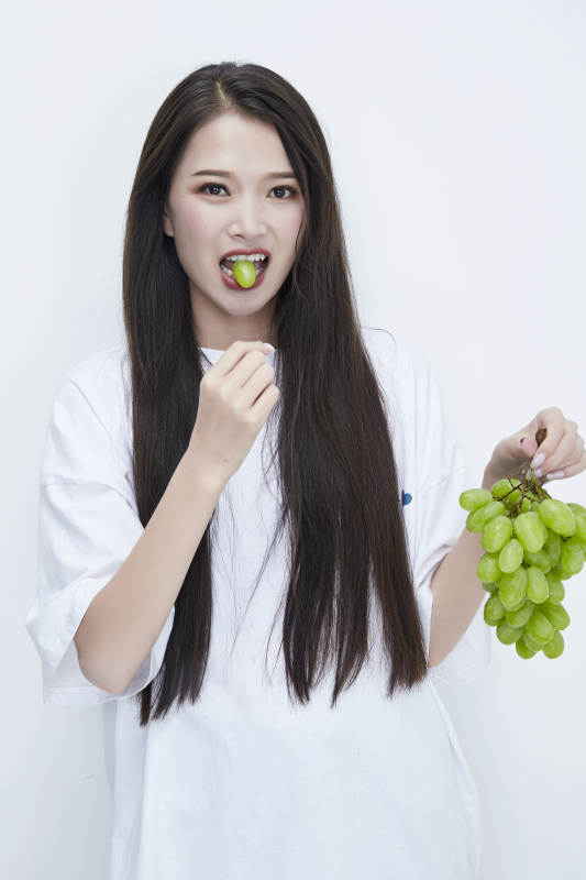 吃葡萄的穿白色长T血衫的长发可爱少女人像图片