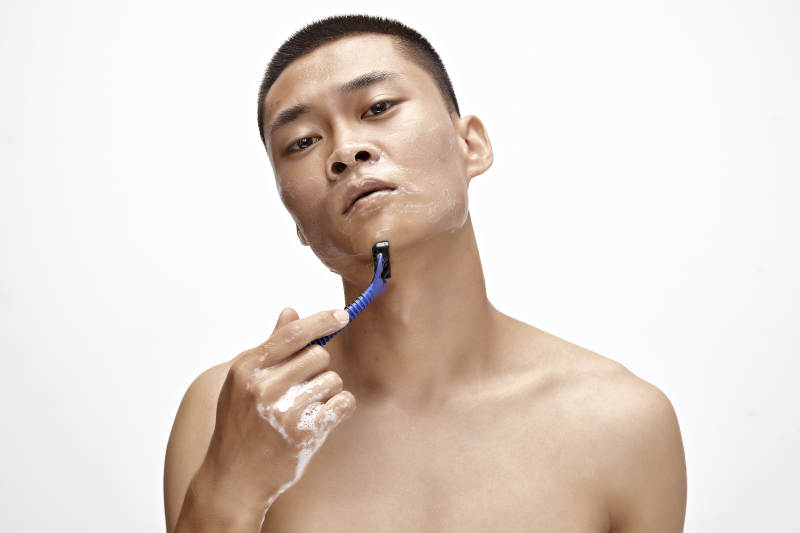 白色背景下手持剃须刀在刮胡子的亚洲男性图片