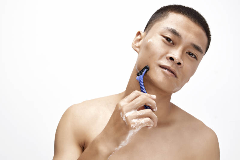 白色背景下手持剃须刀在刮胡子的亚洲男性图片