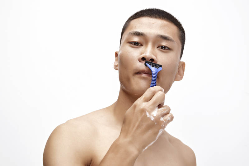 白色背景下手持剃须刀在刮胡子的亚洲男性图片