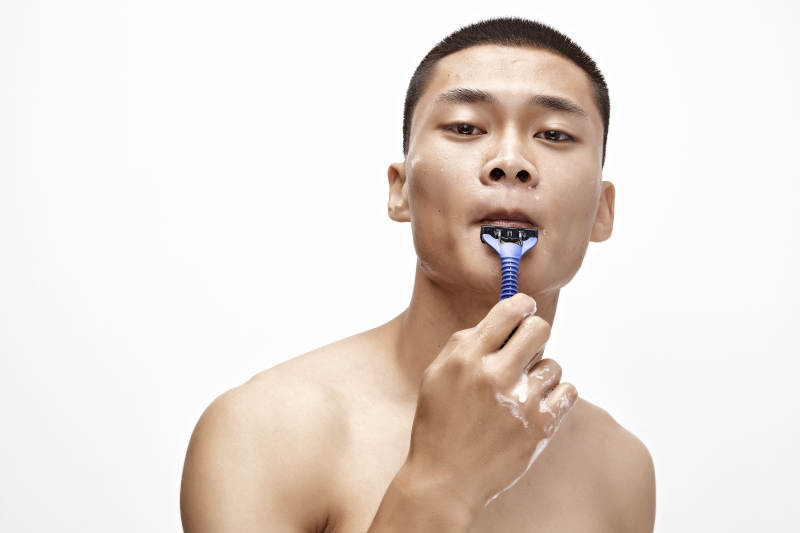 白色背景下手持剃须刀在刮胡子的亚洲男性图片