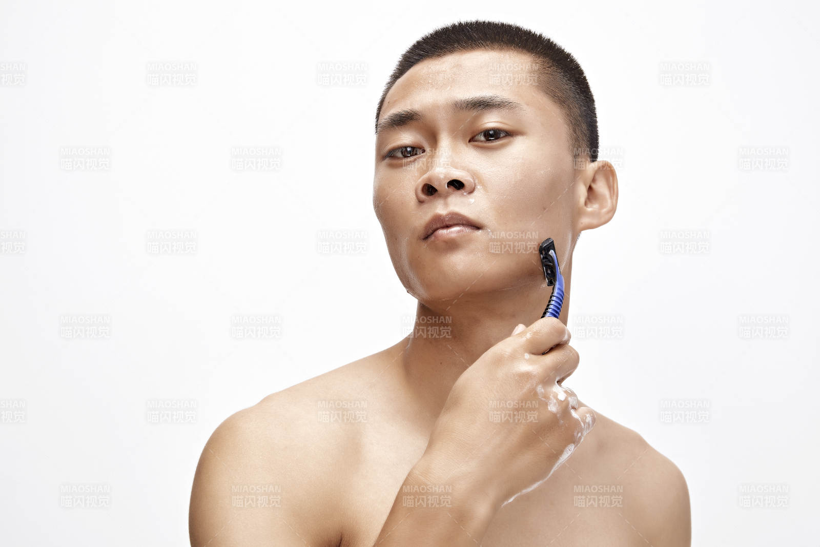 白色背景下手持剃须刀在刮胡子的亚洲男性图片