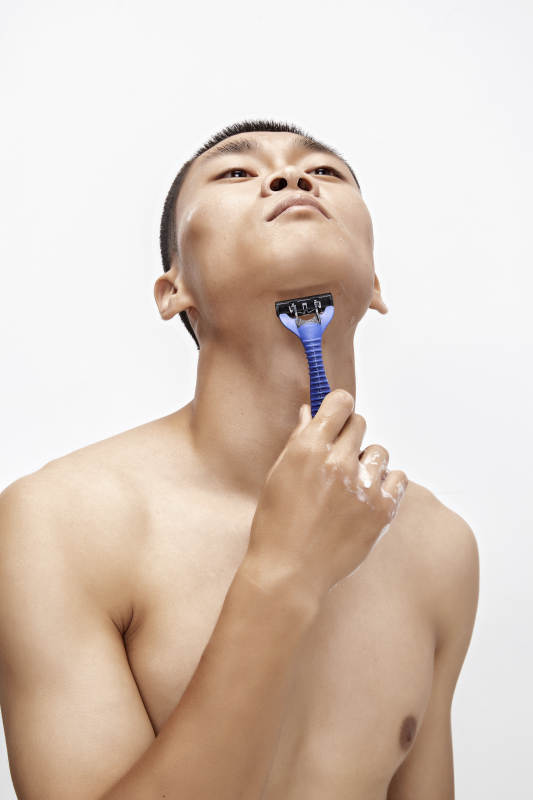 白色背景下手持剃须刀在刮胡子的亚洲男性图片