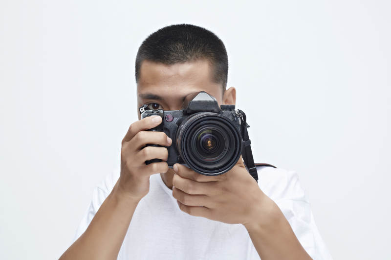 白色背景下手持照相机的亚洲男性摄影师图片