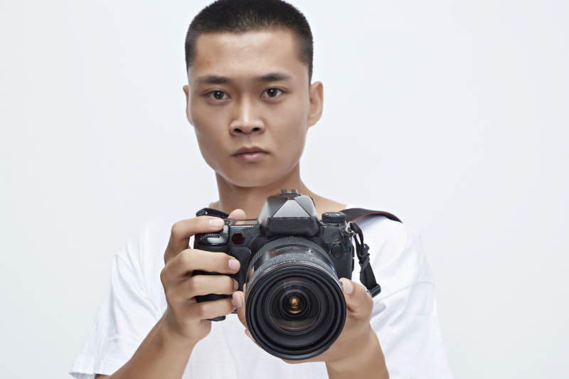 白色背景下手持照相机的亚洲男性摄影师图片