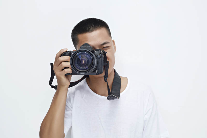 白色背景下手持照相机的亚洲男性摄影师图片