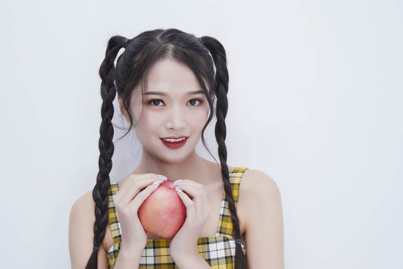 手拿苹果身穿格子吊带裙的亚洲可爱少女人像图片